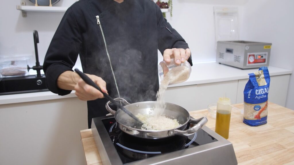 Num tacho quente junte o azeite e refogue a cebola picada e o alho. Junte o arroz e mexa para fritar ligeiramente.